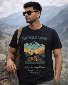 Man wearing a t-shirt with a mountain graphic and text, standing against a mountainous background.